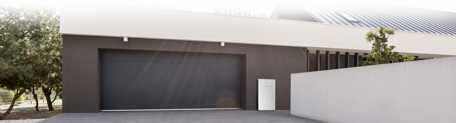 A home battery mounted beside the garage of a modern house